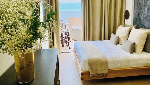 A bedroom with a bed, a bedside table, a vase with flowers, and a view of the beach.
