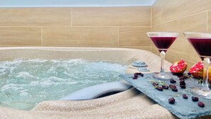 A hot tub with two martini glasses filled with a purple drink, surrounded by pomegranate halves and dried fruits.