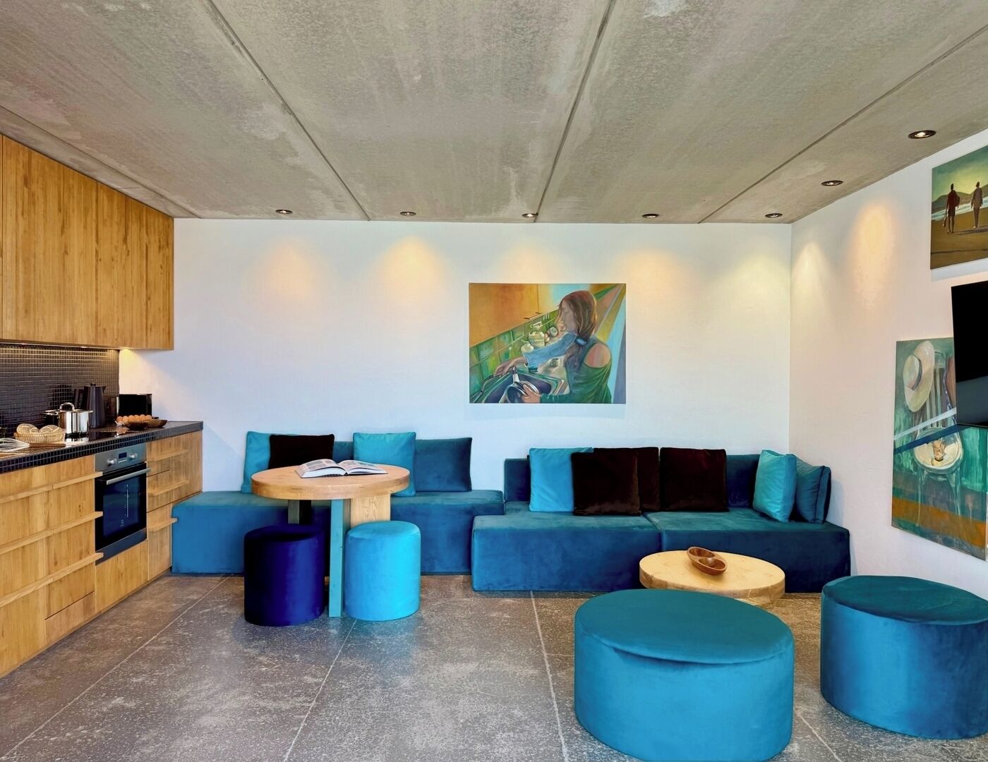 Un espace de vie moderne comprenant une cuisine, un coin salon bleu et des œuvres d’art accrochées aux murs.