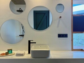 Une salle de bain avec un lavabo blanc, trois miroirs, une porte et une fenêtre.