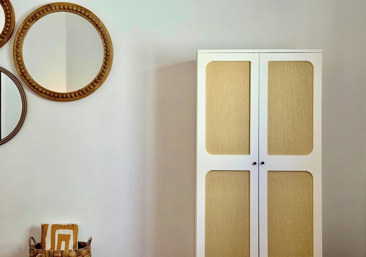 Une pièce avec une armoire blanche dotée de quatre panneaux recouverts d’un tissu texturé. Deux miroirs ronds, encadrés de bois, sont accrochés au mur.