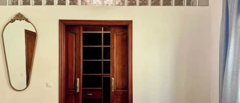 A bedroom with a wooden wardrobe, a mirror, and a window with frosted glass.