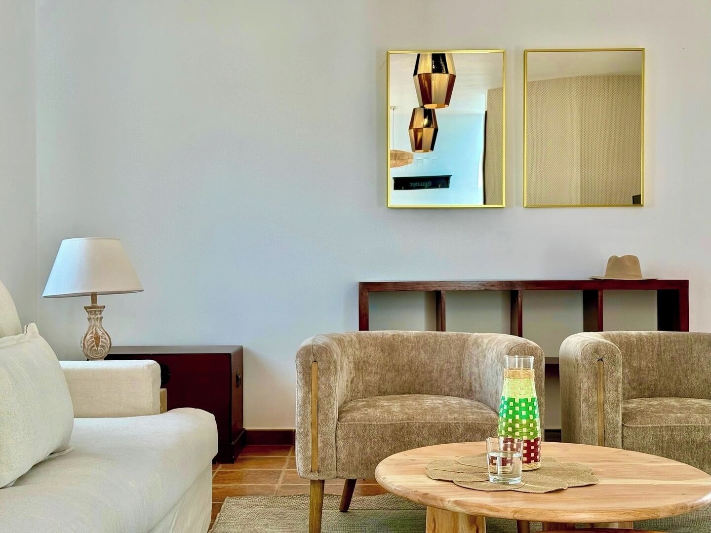 A living room with a sofa, two armchairs, a wooden coffee table, a lamp, and two framed pictures on the wall.