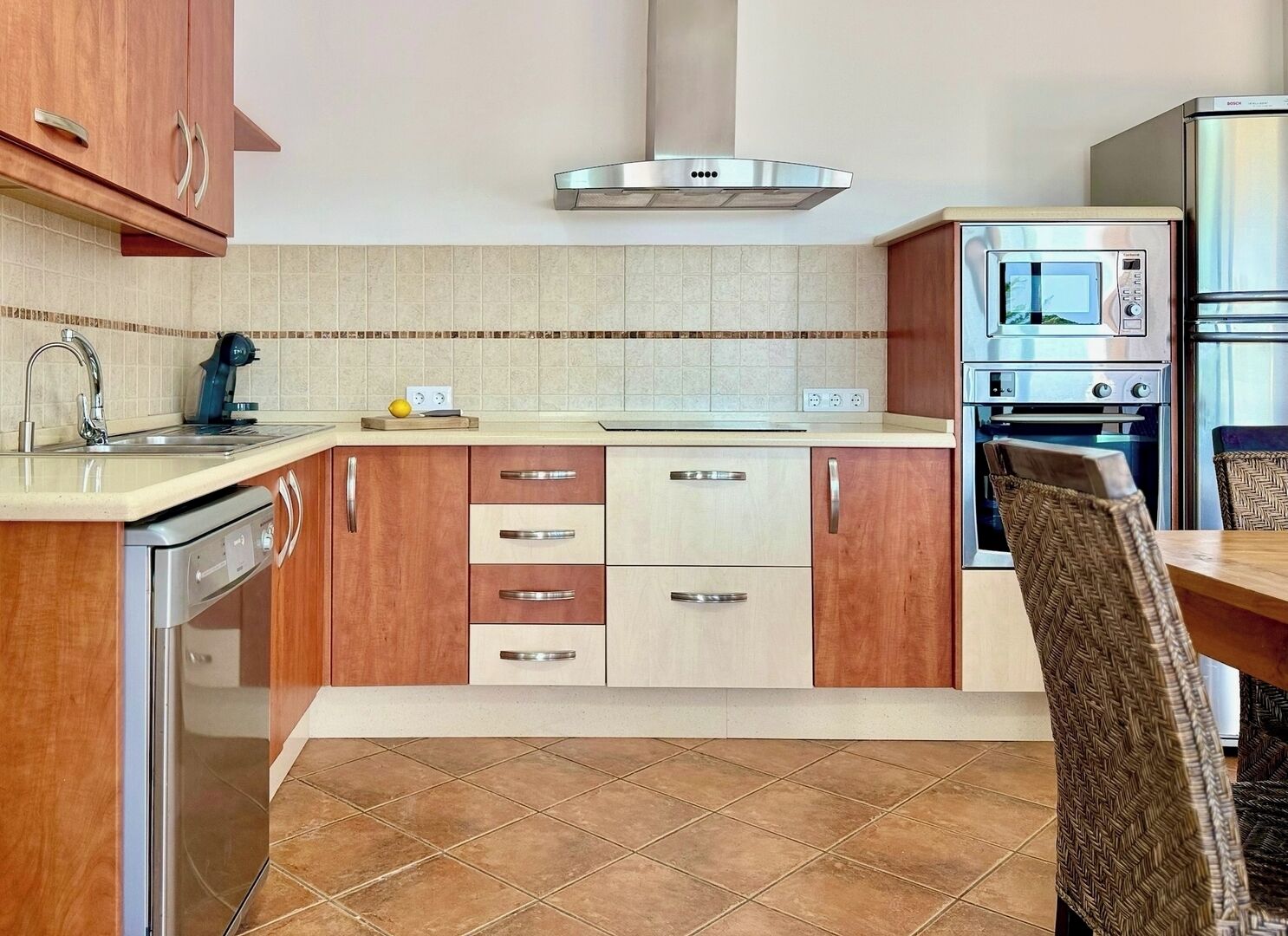 A compact kitchen with wooden cabinets, a stainless steel range hood, a built-in oven, and a dishwasher.