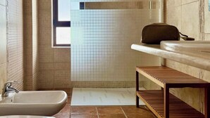 Un baño moderno con bañera, ducha y lavamanos. Hay una ventana que proporciona luz natural y un banco de madera.