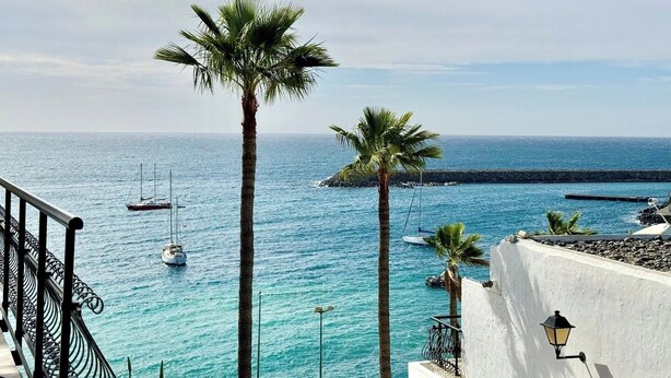A coastal view with clear blue waters, a white building with a balcony, and a palm tree. - Canaryislandshost I Marina (Barranco de la Verga)