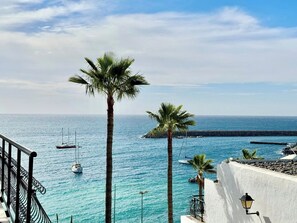 Une vue sur la côte, avec une eau d’un bleu limpide, un bâtiment blanc doté d’un balcon et un palmier.