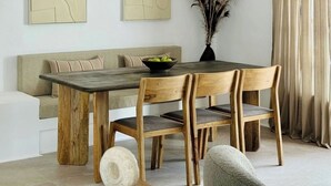 A dining area with a wooden table, six chairs, a bowl of fruit, a vase with dried plants, and two abstract paintings on the wall. - Canaryislandshost l Las Palmeras (Nazaret)
