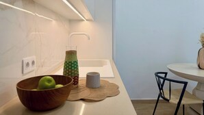 Une cuisine moderne avec un pare-feu en marbre, un saladier en bois contenant des pommes vertes, une bouteille d’eau tressée et une table ronde avec des chaises.