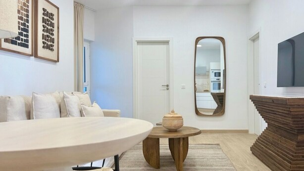 Un salon moderne avec une table à manger ronde, un canapé, une table basse en bois, un grand miroir et un téléviseur fixé au mur.