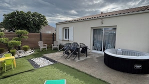 Un patio trasero con césped artificial, un jacuzzi, mobiliario de exterior y una mesa de patio.