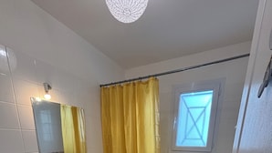 Un baño con lavamanos blanco, espejo, cortina de ducha amarilla y una ventana sobre la bañera.