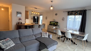 Una sala de estar moderna con un sofá seccional gris, una mesa de comedor con sillas, una zona de cocina y un acuario.
