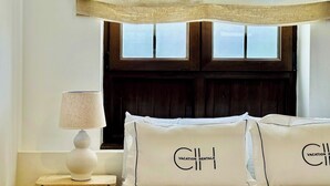 Ein Schlafzimmer mit einem Bett, einem Nachttisch, einer Lampe und einem Fenster mit Holz-Kopfteil.