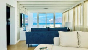 Een moderne woonkamer met een bank, een salontafel met tijdschriften, een televisie en een groot raam met uitzicht op zee.