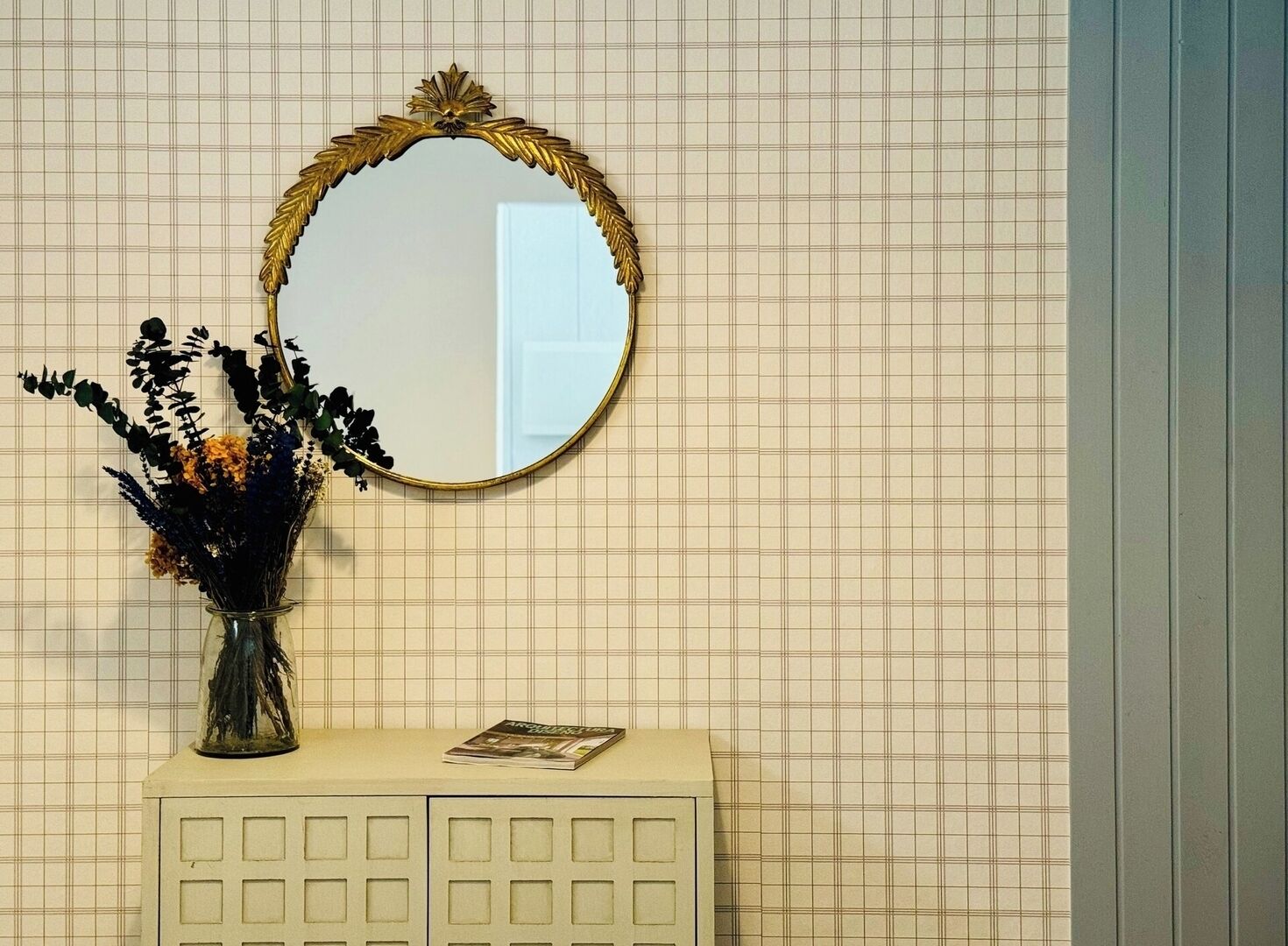 A bathroom with a mirror, a vase with flowers, and a magazine on the counter.