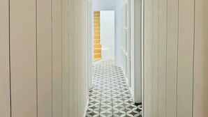 Een hal met een vloer met geometrisch patroon, witte muren en een deur die leidt naar een kamer met een houten trap.