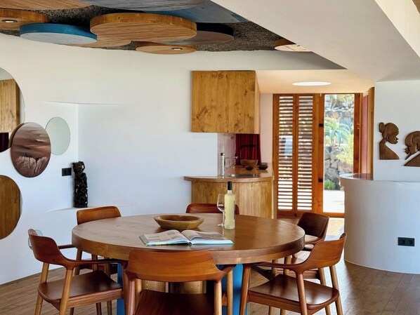 Un espace repas moderne avec une table ronde en bois, six chaises en bois et un grand saladier au centre.