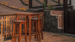 Un balcon avec une table et des chaises en bois, donnant sur un paysage volcanique parsemé de champs en terrasses.
