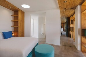 Une chambre moderne avec un lit, un oreiller bleu, un pouf rond et des étagères en bois.