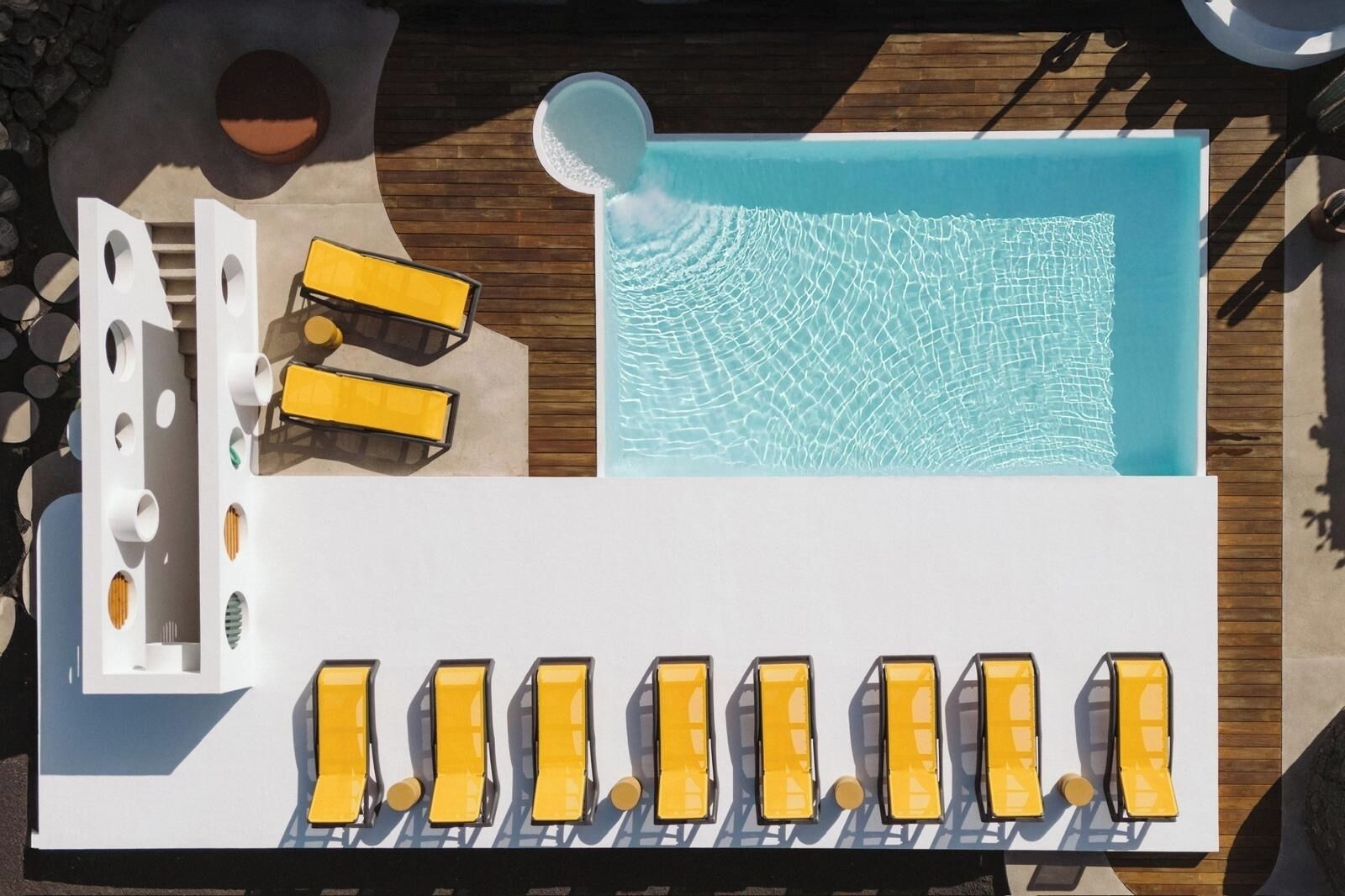 Ein Pool im Freien mit einer Holzterrasse, gelben Liegestühlen und einem Bereich mit weißen Sonnenliegen.