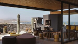 Un espace extérieur moderne aménagé avec des sièges, offrant une vue sur l’océan et les montagnes, et agrémenté de mobilier en bois et de cactus.