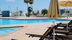 Una piscina con sillas de descanso y sombrillas, rodeada de palmeras y edificios.