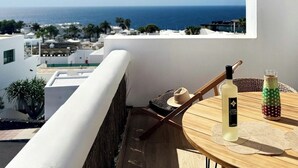 A balcony with a view of the sea, a table with a bottle and a hat, and a wicker chair. - Canaryislandshost l Dalia (Puerto del Carmen)