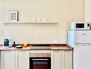 A kitchen with a coffee maker, a microwave, a Brandt refrigerator, a sink, and a countertop with a vase of flowers.