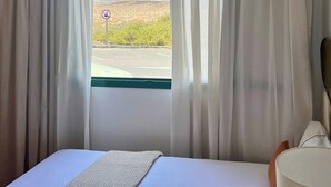 Habitación de hotel con cama, ventana con cortinas y vistas al paisaje desértico.
