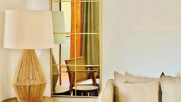 Una habitación con un sofá, una lámpara, un espejo y un taburete de madera.
