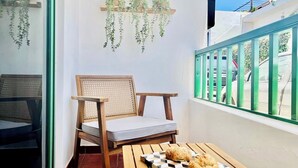 Un balcón con una silla de madera, una mesa con pasteles y plantas colgantes.