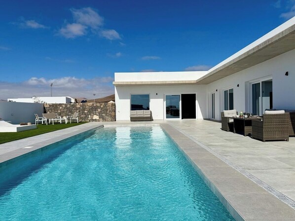 Una casa moderna con piscina, mobiliario de exterior y un muro de piedra.