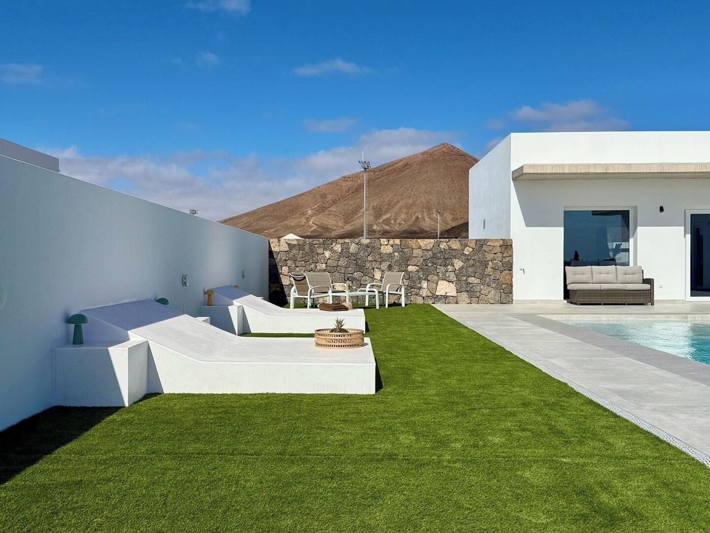 Un espacio exterior moderno con piscina, sillas de descanso blancas y un muro de piedra.