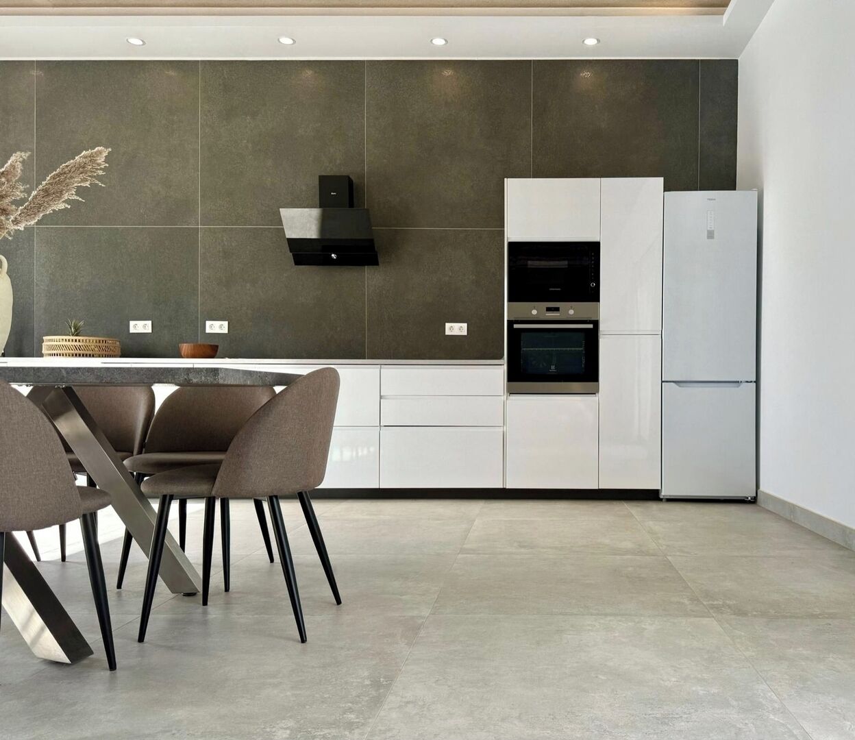 A modern kitchen with white cabinets, a built-in oven, and a stainless steel refrigerator.