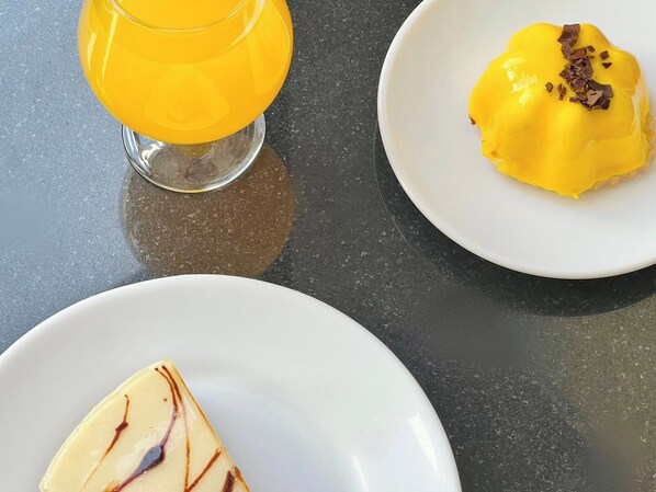 A table with a glass of orange juice, a plate with a dessert topped with chocolate shavings, and a slice of cake with a drizzle of chocolate.