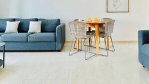 Un salón con un sofá azul, una mesa de comedor con sillas de mimbre y una obra de arte abstracta enmarcada en la pared.