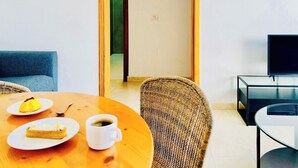 Una habitación moderna con una mesa de comedor de madera, dos sillas, un televisor y un acceso a otra habitación.