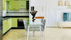 Une cuisine moderne avec des meubles de couleur verte, une table à manger en verre et une porte blanche.