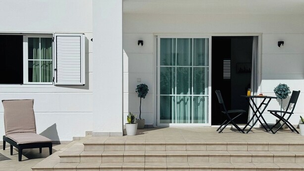 Un bâtiment moderne doté d’un espace extérieur aménagé, abrité et comprenant une table, des chaises et une petite plante en pot.