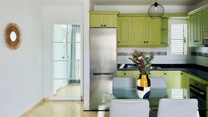 Une cuisine moderne avec des meubles de couleur verte, un réfrigérateur en acier inoxydable et une table à manger en verre.