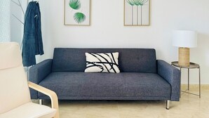 Un salon moderne avec un canapé gris, une lampe blanche posée sur une table d’appoint et deux reproductions botaniques encadrées accrochées au mur.