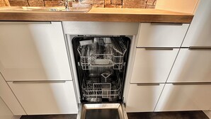 Een open vaatwasser in een keuken met een betegelde achterwand en witte kasten.