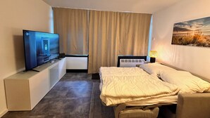 Een hotelkamer met een bed, een televisie op een standaard, een verwarming en een raam met gordijnen.