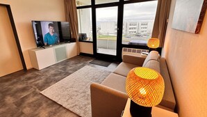 Een moderne woonkamer met een televisie, bank en grote ramen met uitzicht op gebouwen en een straat.
