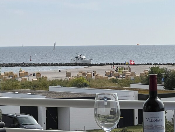 Vista costera con un bote, sillas de playa y una botella de vino en un balcón.