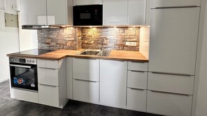 Een moderne keuken met witte kasten, een steenschildering, een houten aanrechtblad en ingebouwde apparatuur.