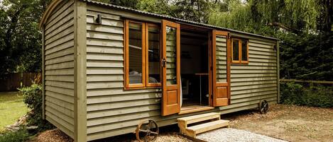 A small, single-story cabin with a front door open, revealing a simple interior.
