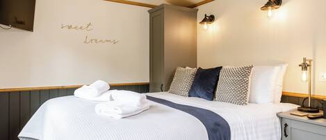 Un lit bien fait, recouvert d’une couverture blanche et bleu marine, une serviette pliée posée sur le lit, et un mur orné d’une inscription « Faites de beaux rêves ».