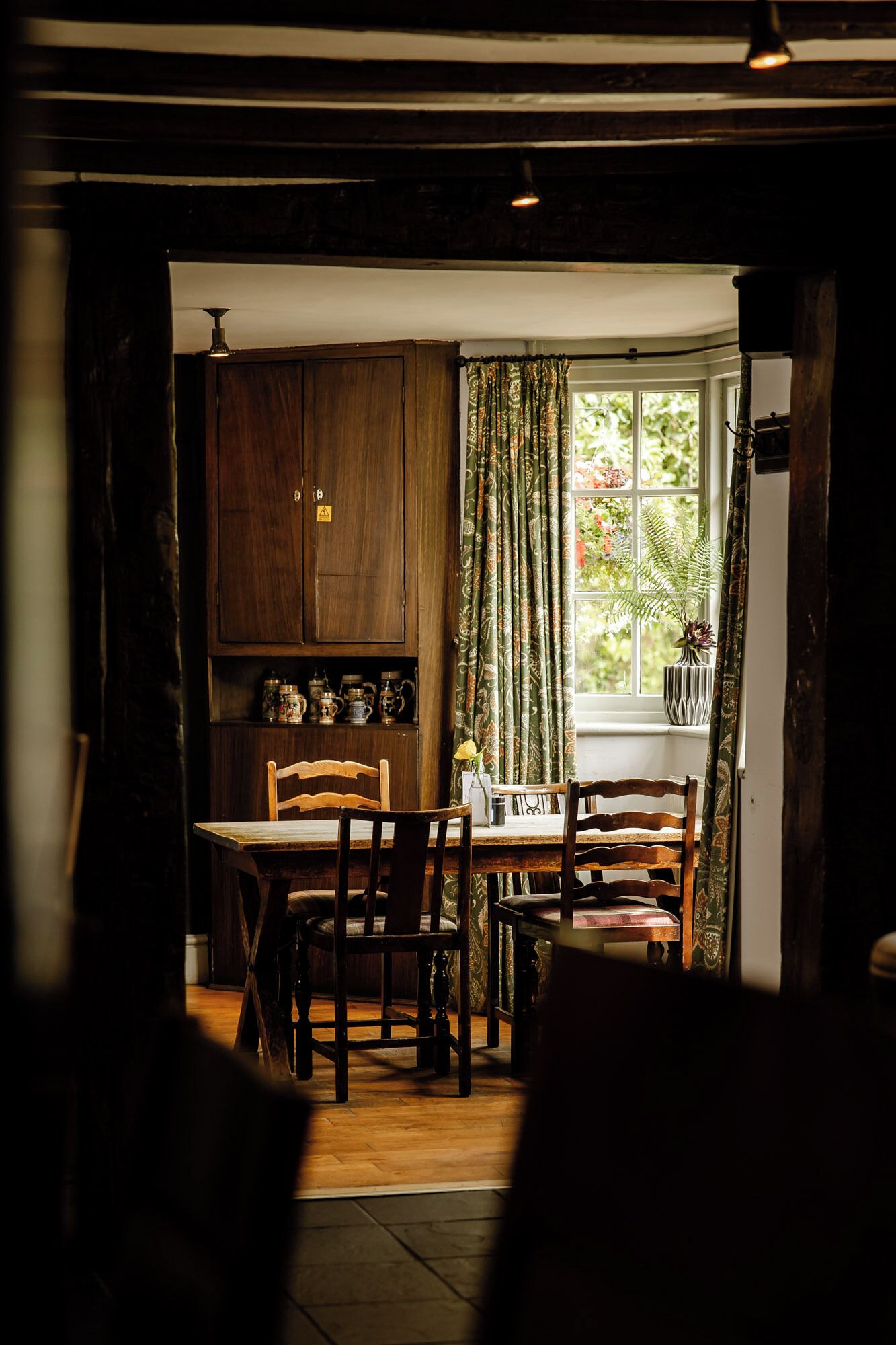 A cozy dining area with wooden furniture, a window with curtains, and a view of greenery outside.
